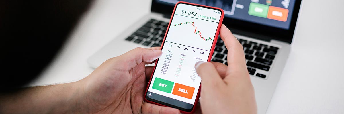 Person trading shares using a laptop and mobile phone
