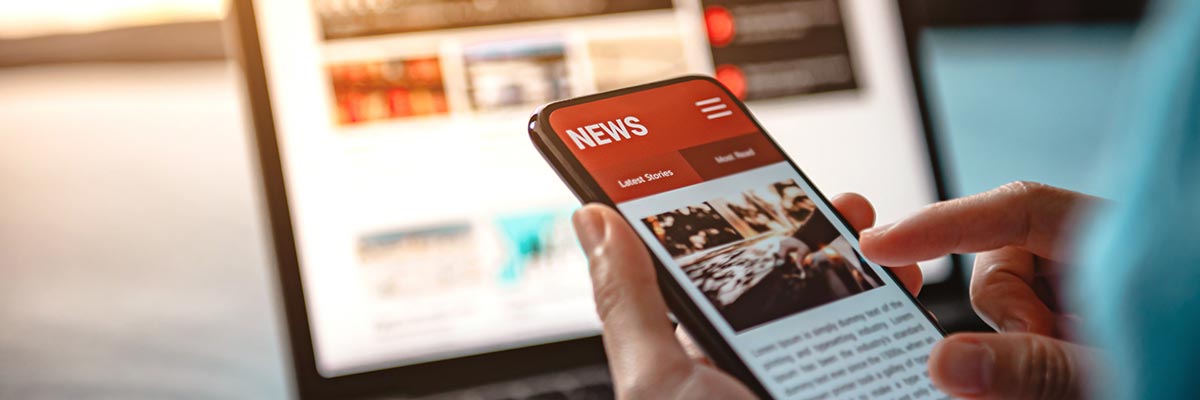 Person reading news online via a laptop and mobile phone