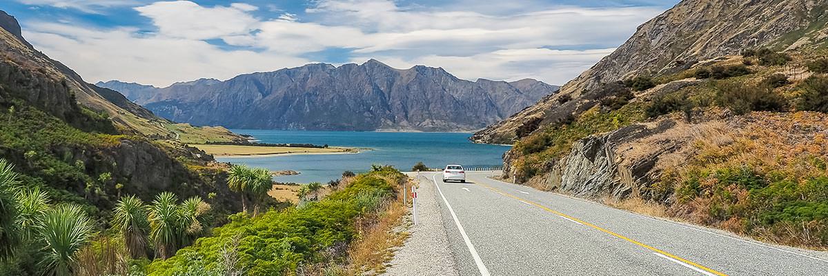 Luxury car driving along a back-country road towards Lake Hawea, Wanaka, with the mountains beyond