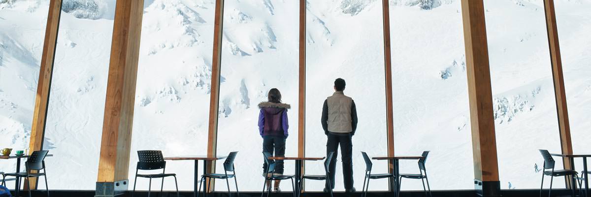 Young couple in front of a large picture window, looking out onto snow-covered mountains