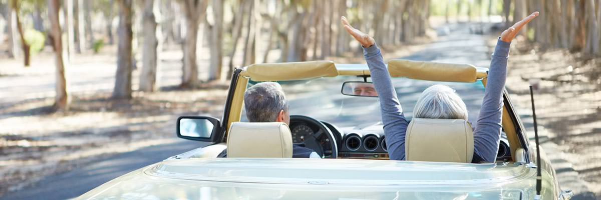 Retired couple in an open-topped sports car, speeding along a country road