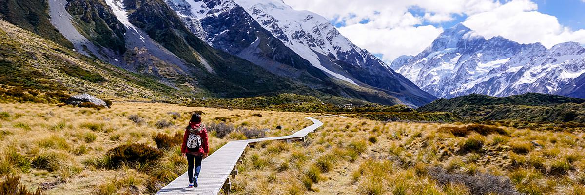 Woman tramping in Aotearoa towards snow-covered mountains