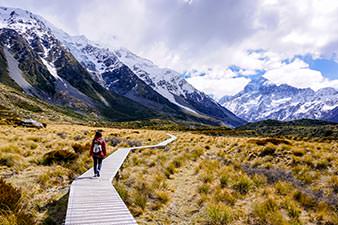 Woman tramping in Aotearoa towards snow-covered mountains
