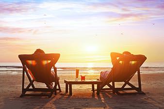 Couple relaxing in deckchairs on the beach, watching the sunset